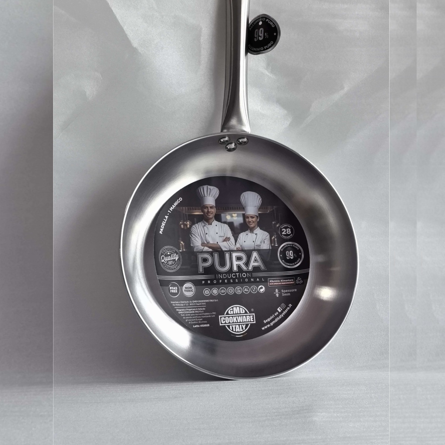 Una padella argentata Pura Induction con etichetta che mostra due chef su sfondo bianco.
