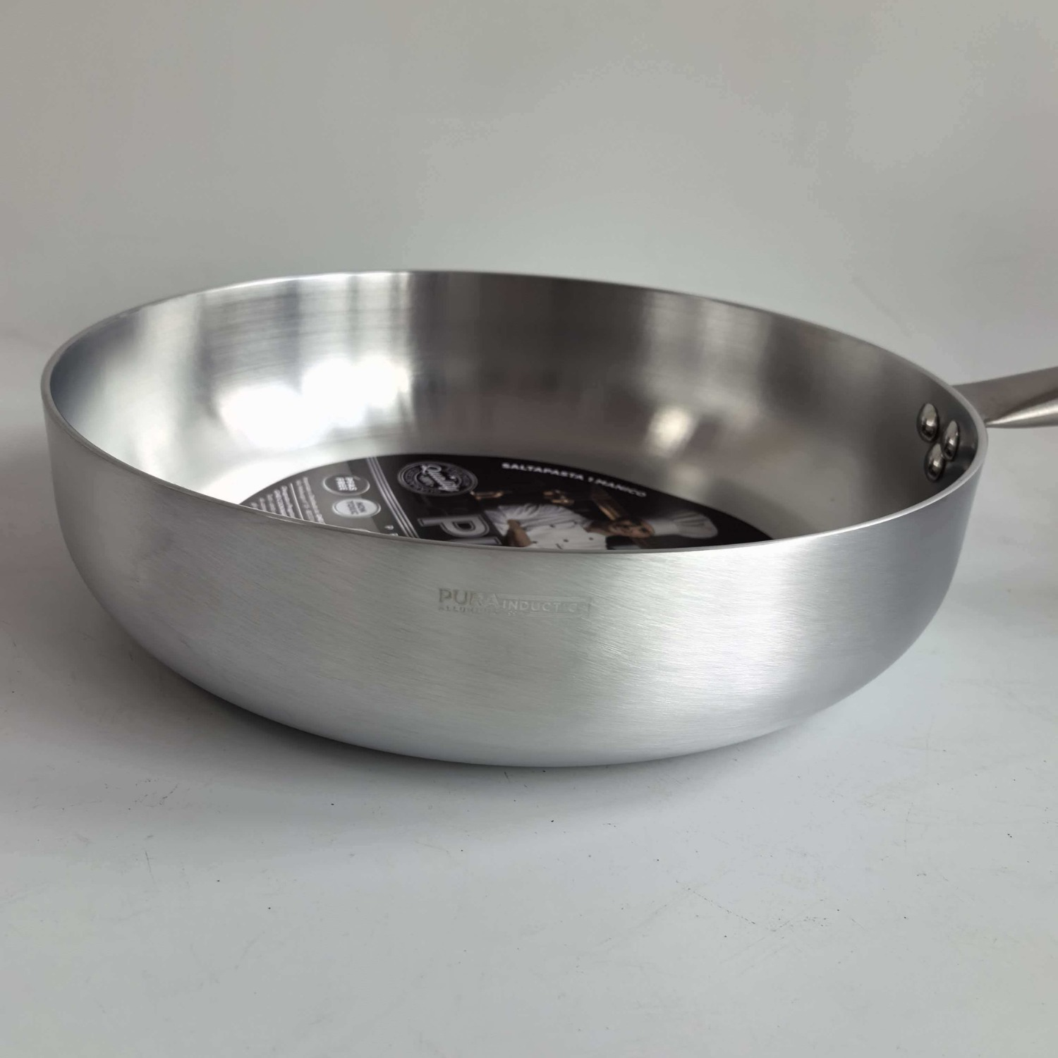 Una padella in alluminio argentato con etichetta interna, su superficie bianca.