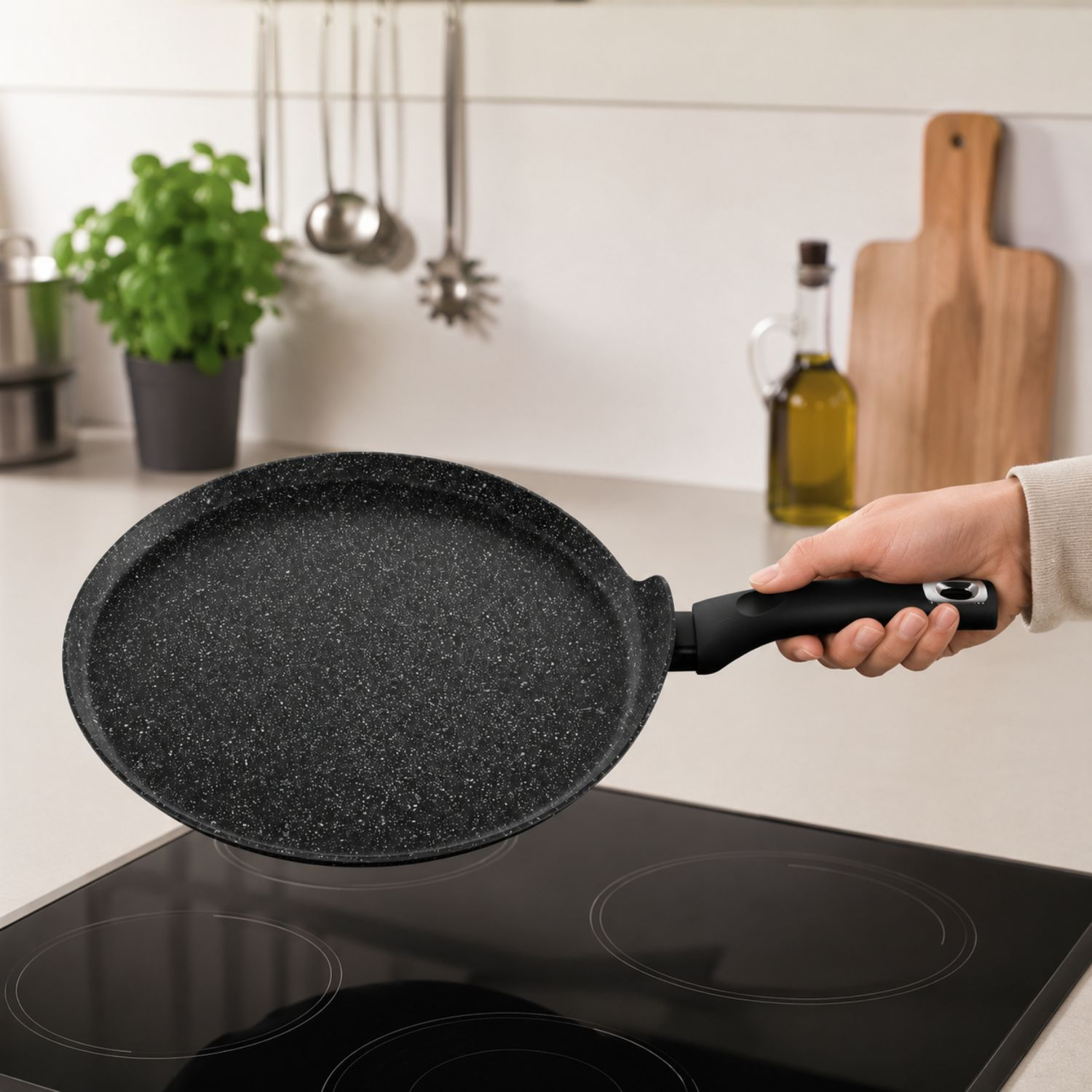 Una mano tiene una padella nera sopra un piano cottura in vetroceramica.
