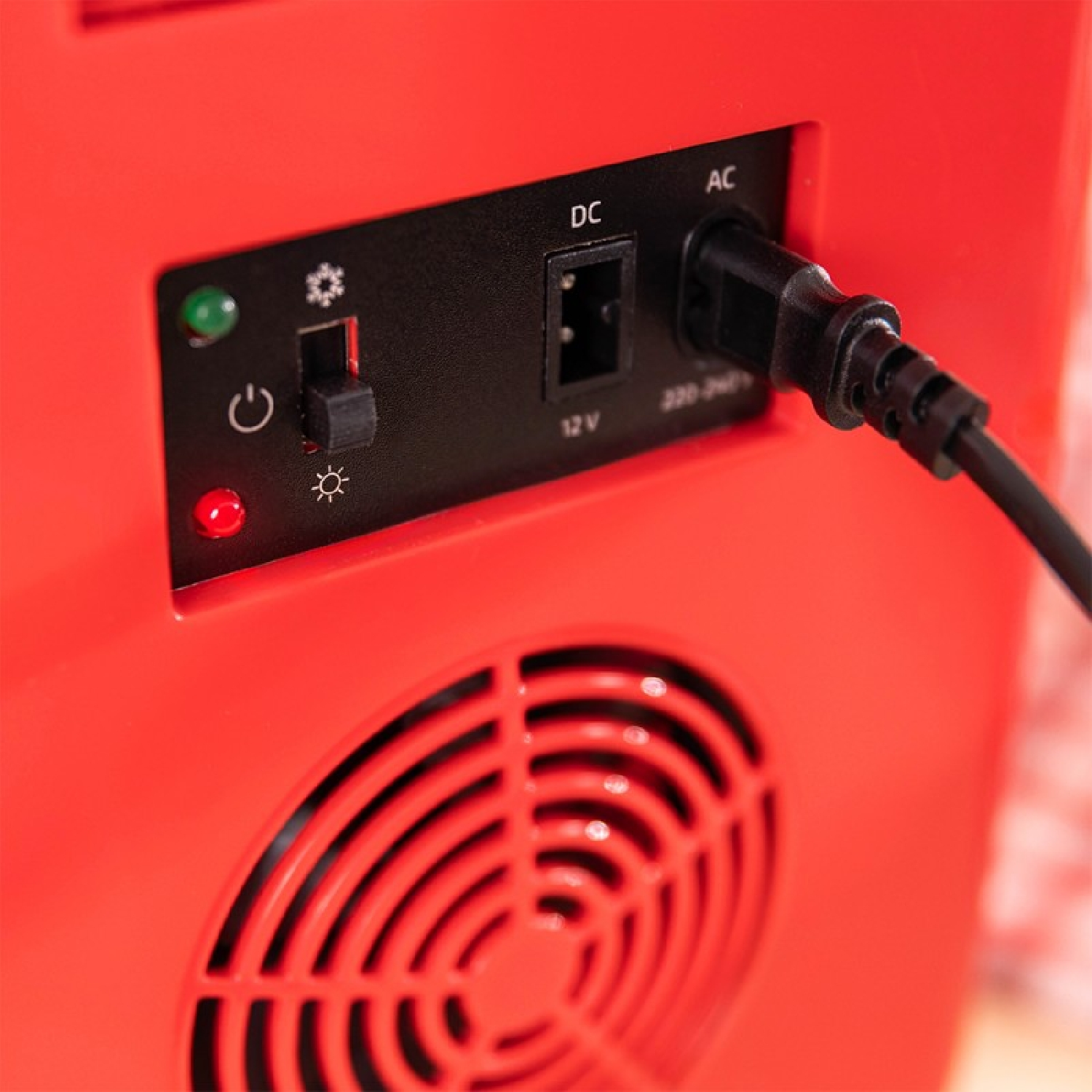 La parte trasera de un dispositivo rojo con un cable de CA, un interruptor y una rejilla circular.