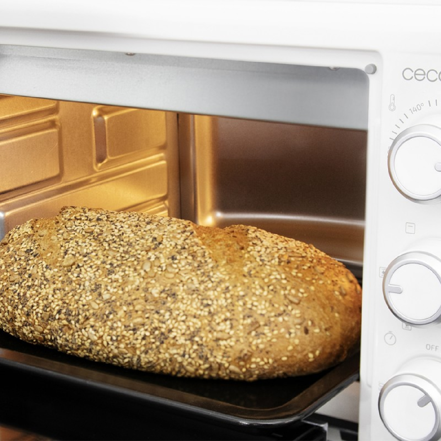 Una pagnotta di pane con semi di sesamo su una teglia in un forno bianco.
