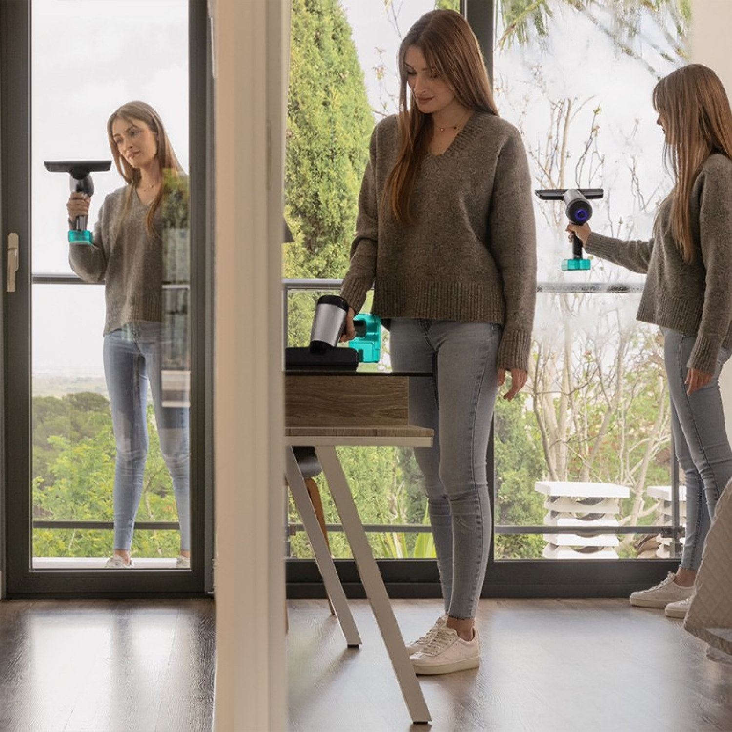 Una donna con maglione grigio e jeans pulisce una porta a vetri con un aspirapolvere portatile in una stanza luminosa.
