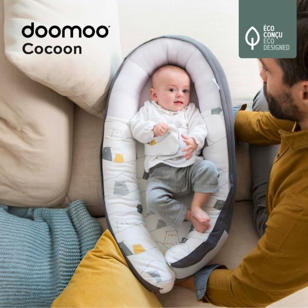 Ein Baby liegt in einem Doomoo Cocoon Babynest, während ein Mann daneben sitzt.