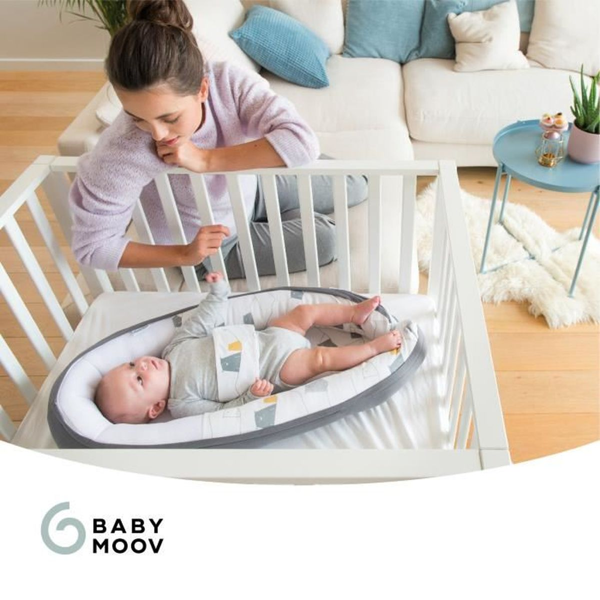 Eine Frau schaut auf ein Baby, das in einem weißen Gitterbett in einem Nest liegt.