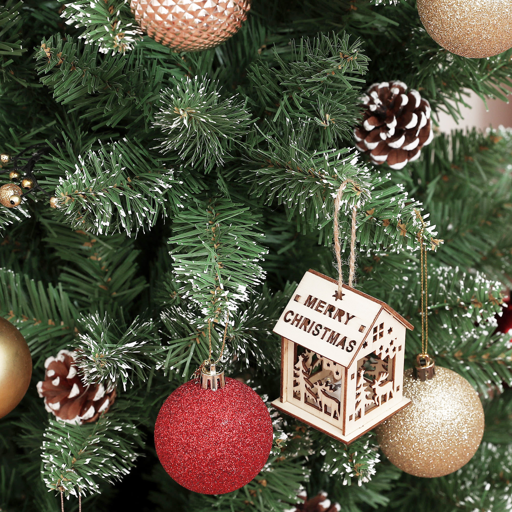 Un árbol de navidad decorado con esferas rojas y doradas, piñas y un pequeño adorno de casa de madera.