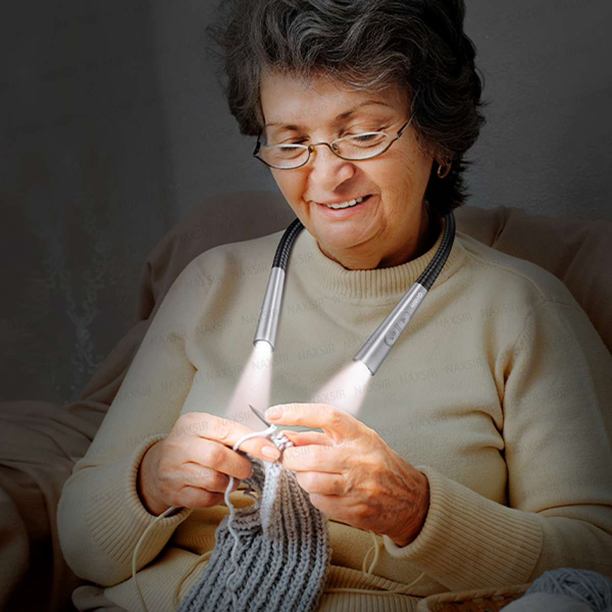 Eine ältere Frau mit Brille trägt eine flexible Nacken-Leselampe und strickt einen grauen Pullover.