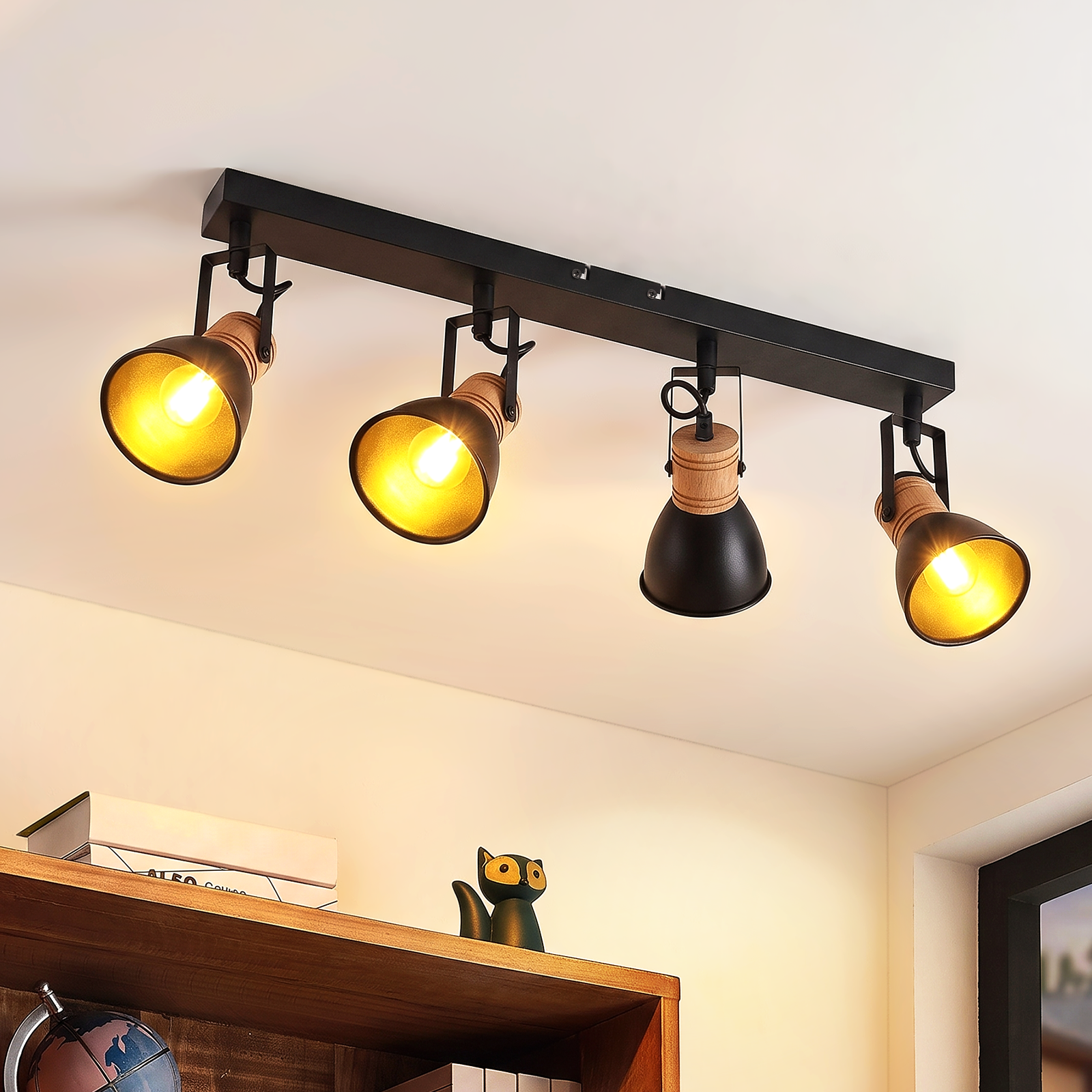 Un foco de techo negro con cuatro luces ajustables sobre un fondo de pared blanca y madera.