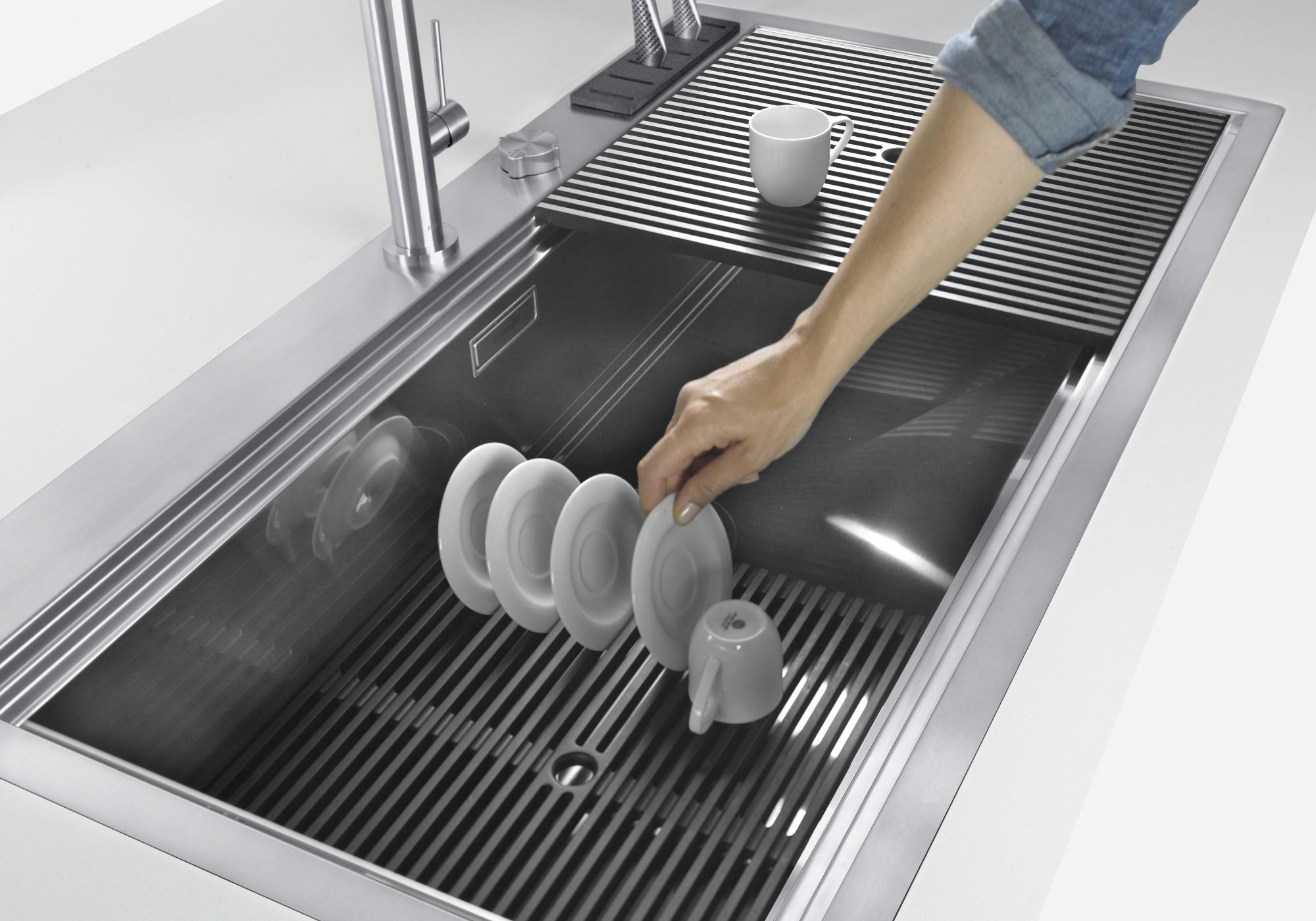Una mano posiziona un piattino in un moderno lavello in acciaio grigio.