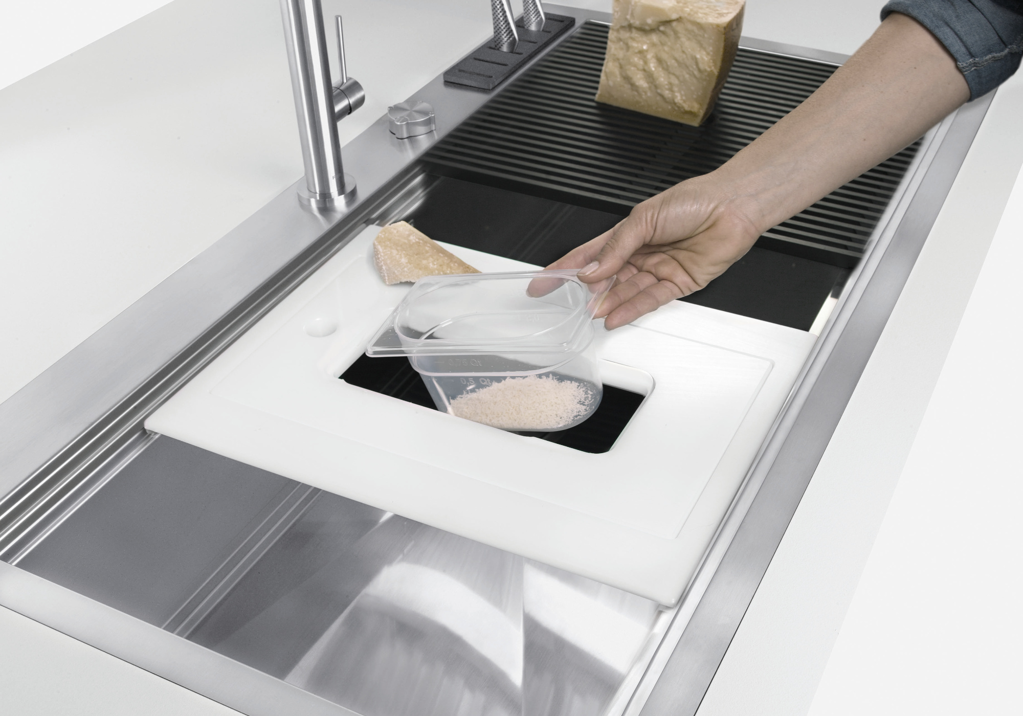 Una persona tiene un contenitore sopra un lavandino su un tagliere bianco, con del formaggio.