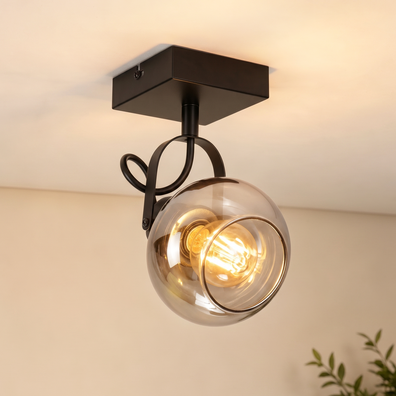 Un foco de techo negro con una pantalla de vidrio redonda de color ahumado y una bombilla iluminada.