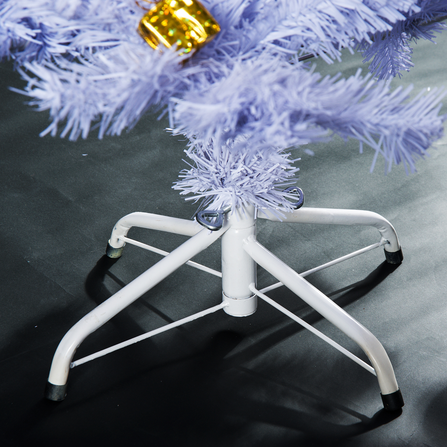 Un soporte de metal blanco sostiene un árbol de Navidad artificial blanco adornado con un adorno dorado.