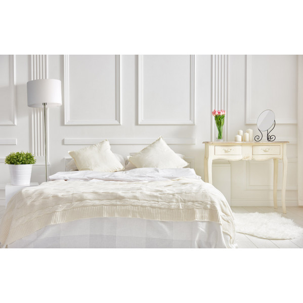 Un dormitorio luminoso con cama blanca, lámpara alta, mesita con tulipanes rosas y espejo ante una pared panelada.