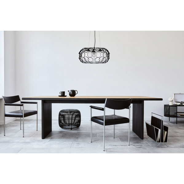 Comedor moderno con mesa larga de madera, sillones de cuero negro, tetera y lámpara colgante redonda.