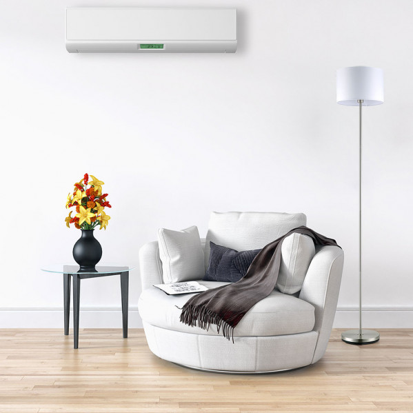 Un sillón blanco con manta, mesa auxiliar con flores, lámpara de pie y aire acondicionado de pared.