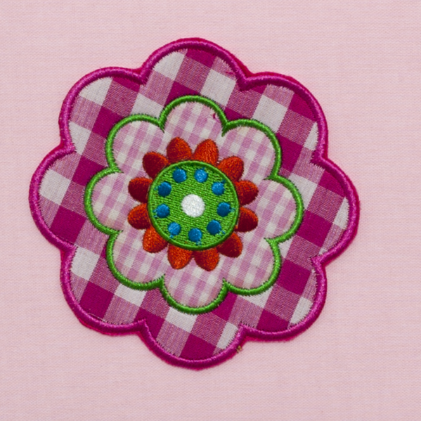 Un parche de tela multicolor en forma de flor con patrón de cuadros sobre fondo rosa.