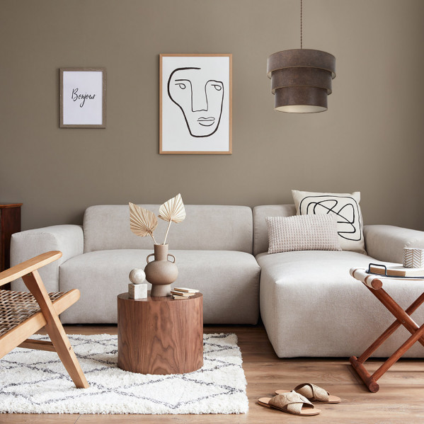 Un sofá sezional beis en una sala con detalles de madera, una mesa de centro redonda y arte abstracto.
