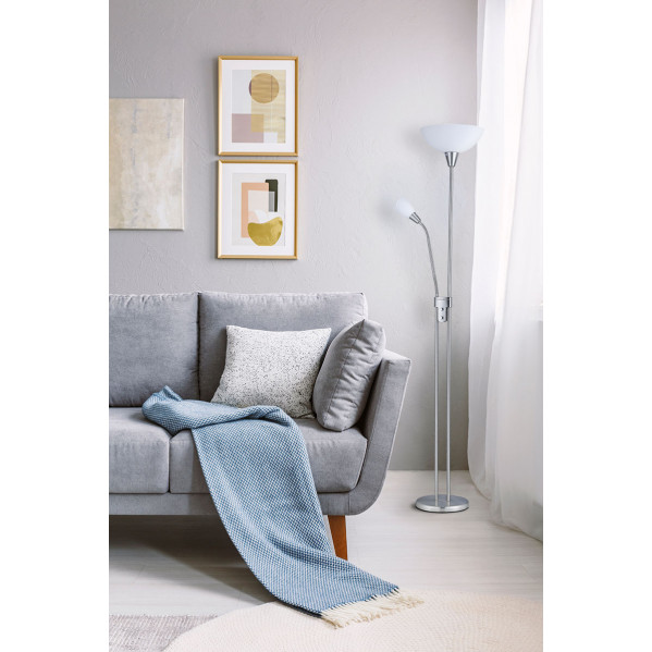 Un sofá gris con manta azul, cojines, lámpara de pie y arte en la pared en una habitación luminosa.