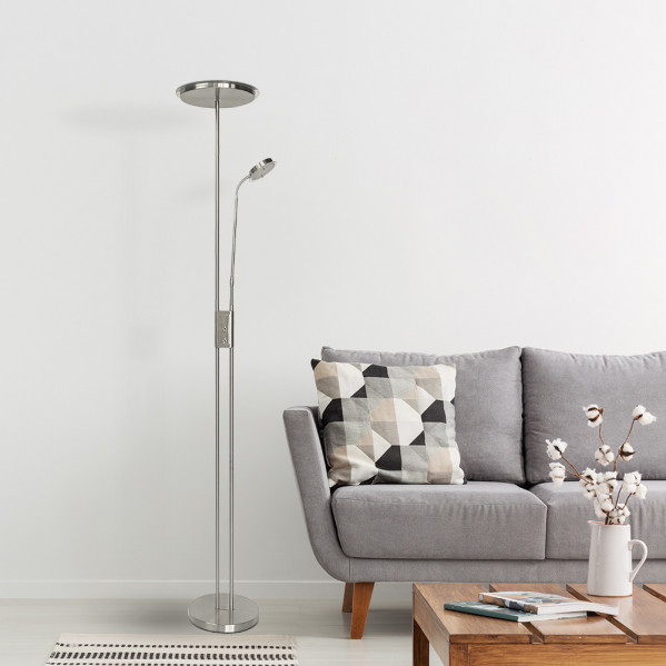 Una lámpara de pie plateada junto a un sofá gris con cojín estampado y mesa de centro con flores.