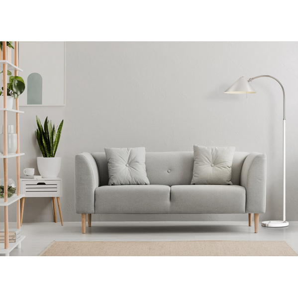 Un sofá gris con dos cojines, una lámpara de pie y una planta en una sala luminosa.