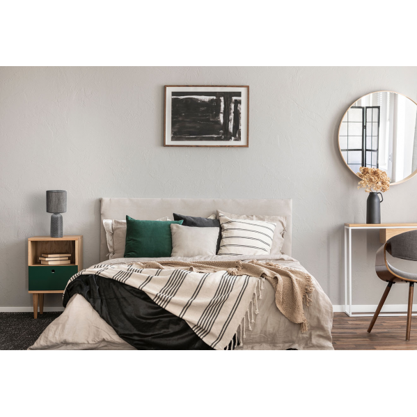 Un dormitorio acogedor con cama gris, cojines verdes, mesita de noche y espejo redondo en pared gris.