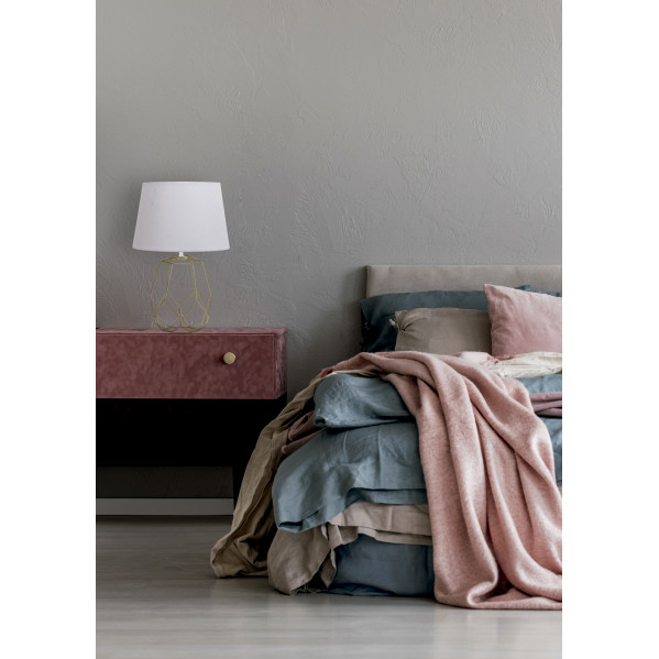 Un dormitorio elegante con una cama gris, cojines rosas, una mesita de noche y una lámpara dorada.