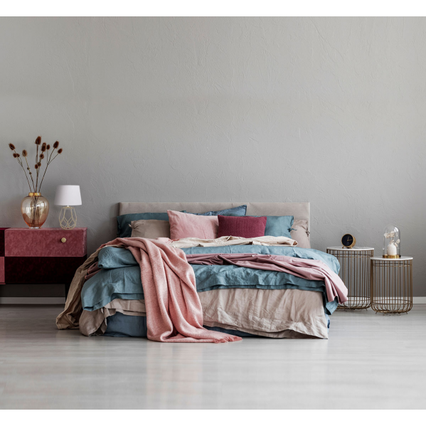 Dormitorio acogedor con cama gris, ropa de cama azul y rosa, mesitas de noche y pared gris.