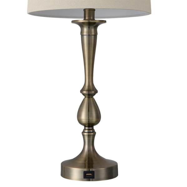 Una lámpara de mesa metálica con soporte de latón y pantalla beige sobre fondo blanco.