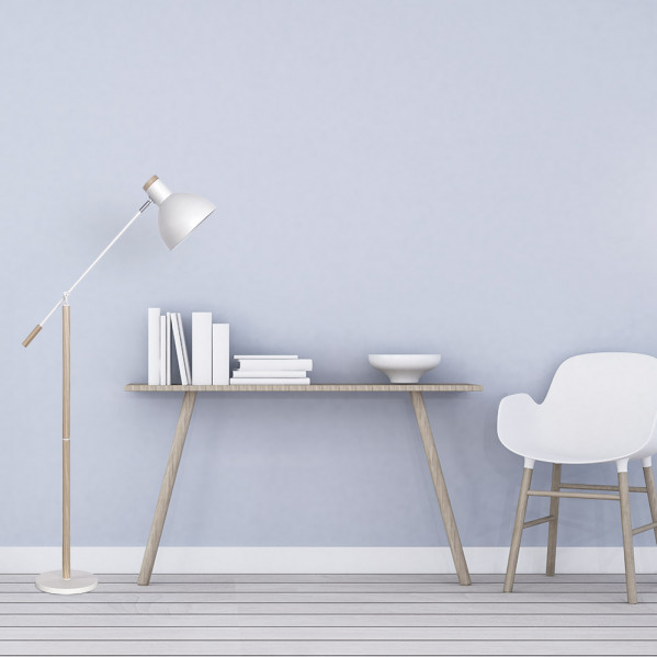 Una habitación minimalista con un escritorio de madera, lámpara de pie, libros alineados, un cuenco y una silla blanca.