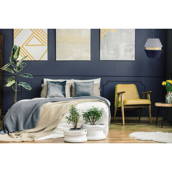 Dormitorio elegante con paredes azul oscuro, cama con mantas grises y beiges, sillón amarillo y arte abstracto.