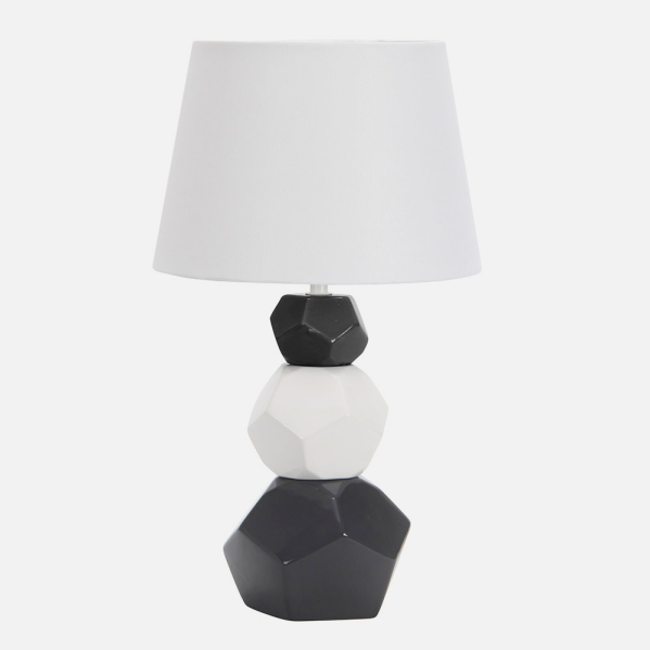 Una lámpara de mesa con pantalla blanca y base de formas facetadas apiladas en blanco y negro.