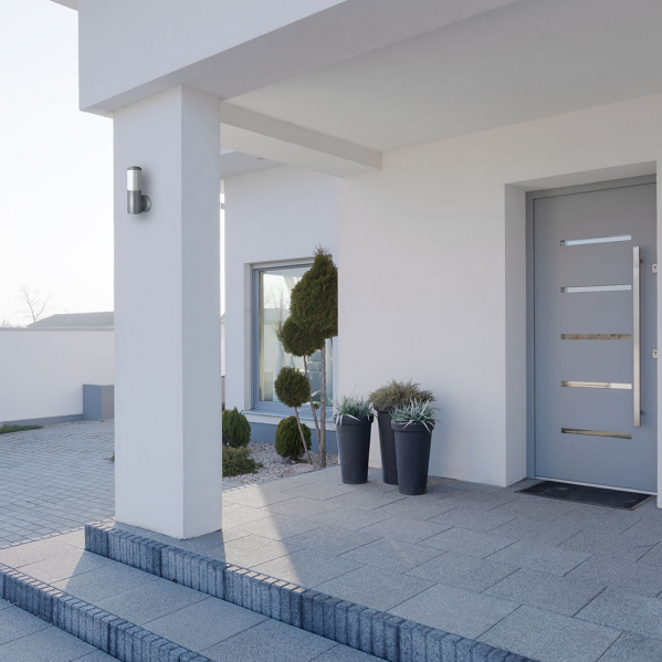 Fachada de casa blanca moderna con puerta gris, aplique de pared y macetas en la entrada.