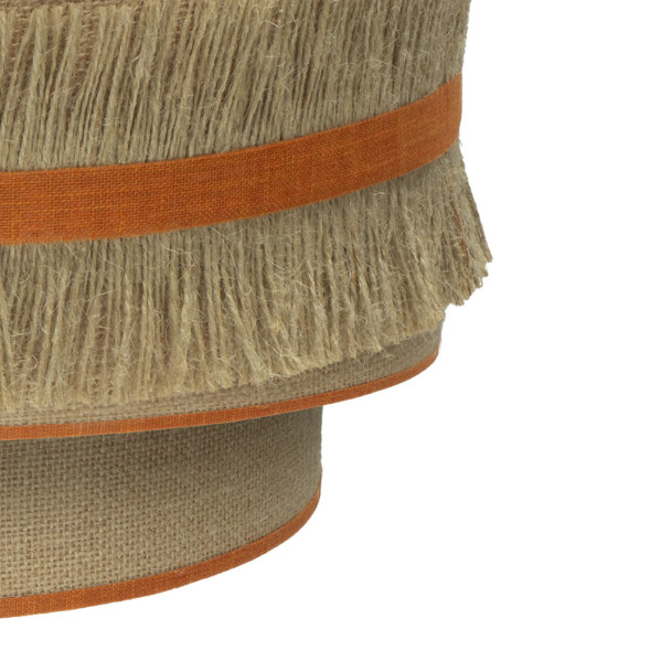 Primer plano de una pantalla de lámpara en capas de arpillera beige con flecos y ribete de tela naranja sobre fondo blanco.