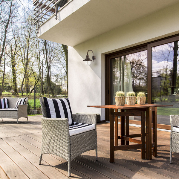 Una terraza moderna de madera con un sillón de mimbre, una mesa plegable con tres cactus y un aplique.