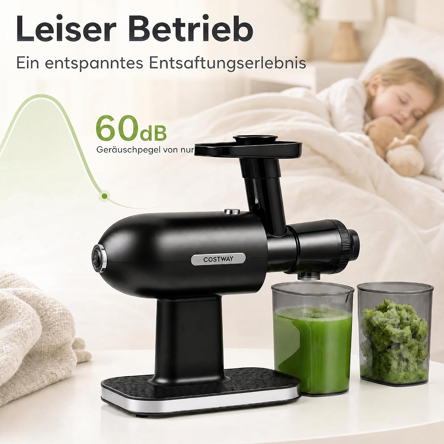 Schwarzer Entsafter auf einem Tisch, daneben grüner Saft und Trester, im Hintergrund schläft ein Kind.