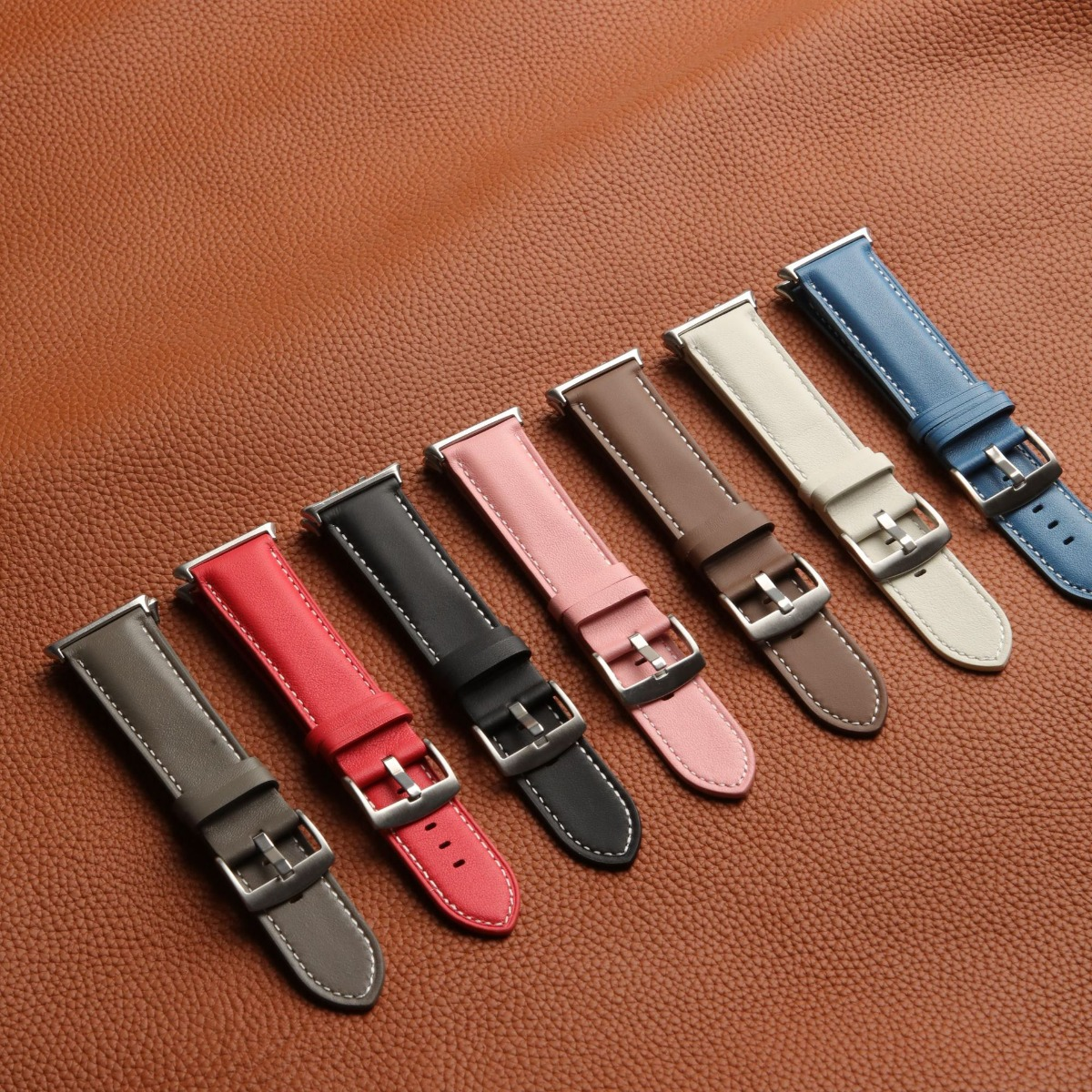 Sieben farbige Lederarmbänder sind diagonal auf strukturiertem braunem Leder angeordnet.