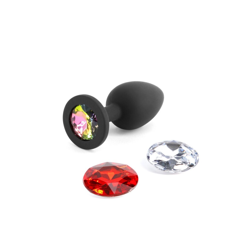 Ein schwarzer Analplug mit einem bunten Juwel und zwei separaten roten und klaren Diamanten.