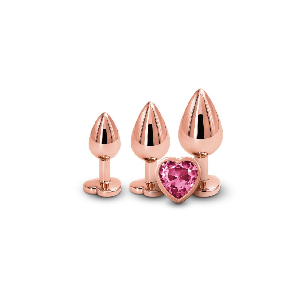 Drei roségoldene Butt Plugs mit flachen Sockeln, der größte ist vorne mit einem facettierten rosa Herz verziert.