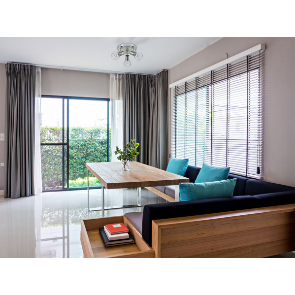 Interior moderno con mesa de comedor de madera, sofá negro, cojines coloridos, ventanas con persianas y cortinas.