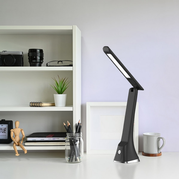 Una lámpara de escritorio LED negra sobre una mesa blanca al lado de una taza y un estante.