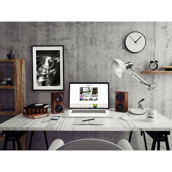 Moderno escritorio con portátil, altavoces, lámpara, libros y un cuadro en blanco y negro enmarcado.