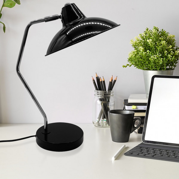 Una lámpara de escritorio negra sobre una mesa blanca junto a una tableta, taza, lápices y planta.