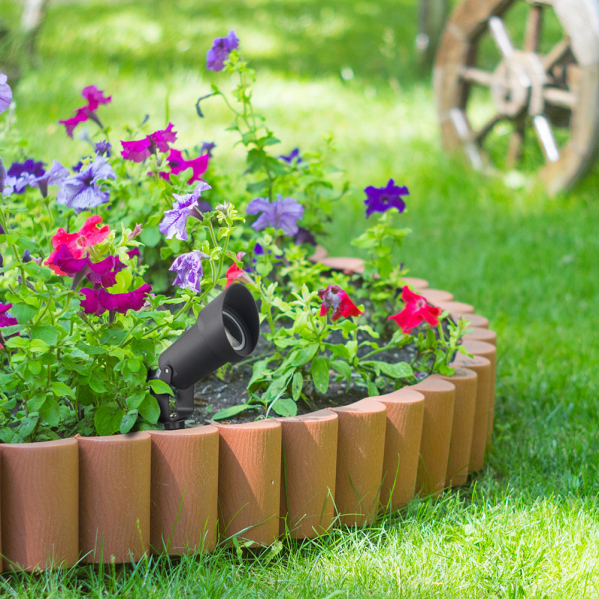 Un pequeño foco de jardín negro en un parterre redondo con flores coloridas y un borde de madera.