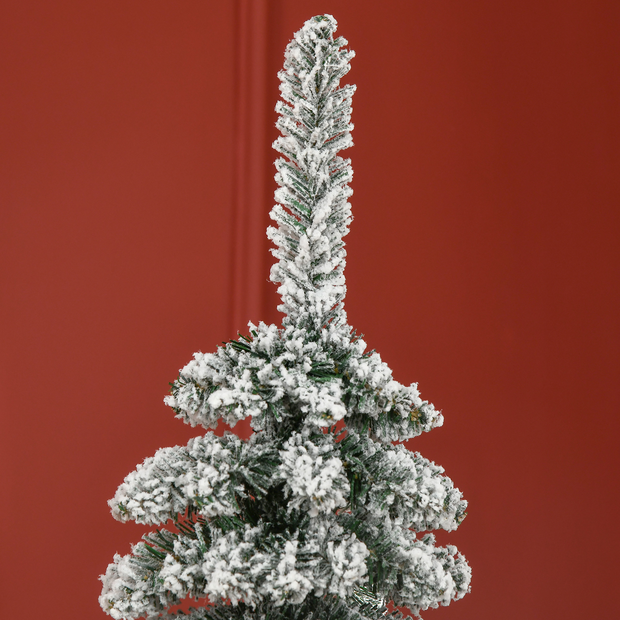 Un árbol de Navidad artificial cubierto de nieve frente a una pared roja.