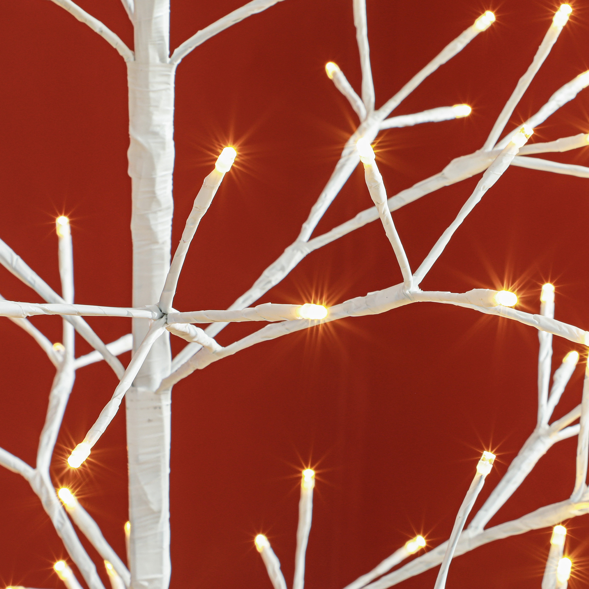 Un árbol blanco iluminado con luces cálidas en sus ramas sobre un fondo rojo.