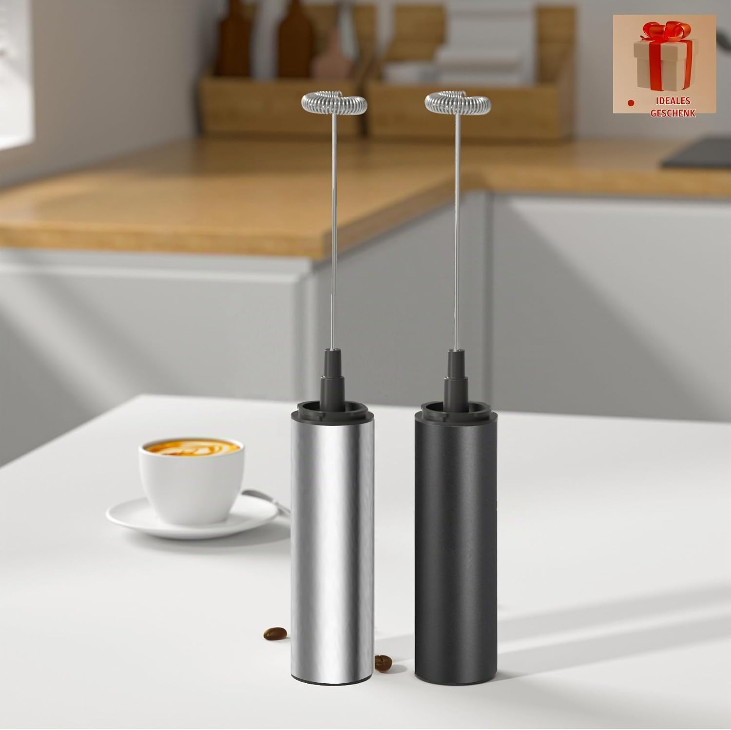 Silberne und schwarze Milchaufschäumer stehen in einer modernen Küche auf einem weißen Tisch mit Kaffeetasse und Bohnen.