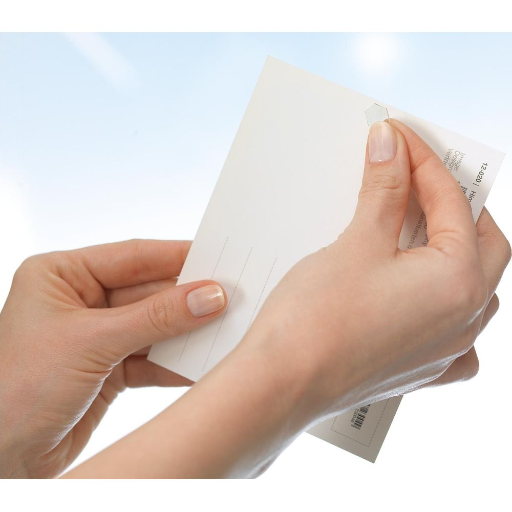 Hände halten eine weiße Postkarte mit Linien und einem kleinen Aufkleber.