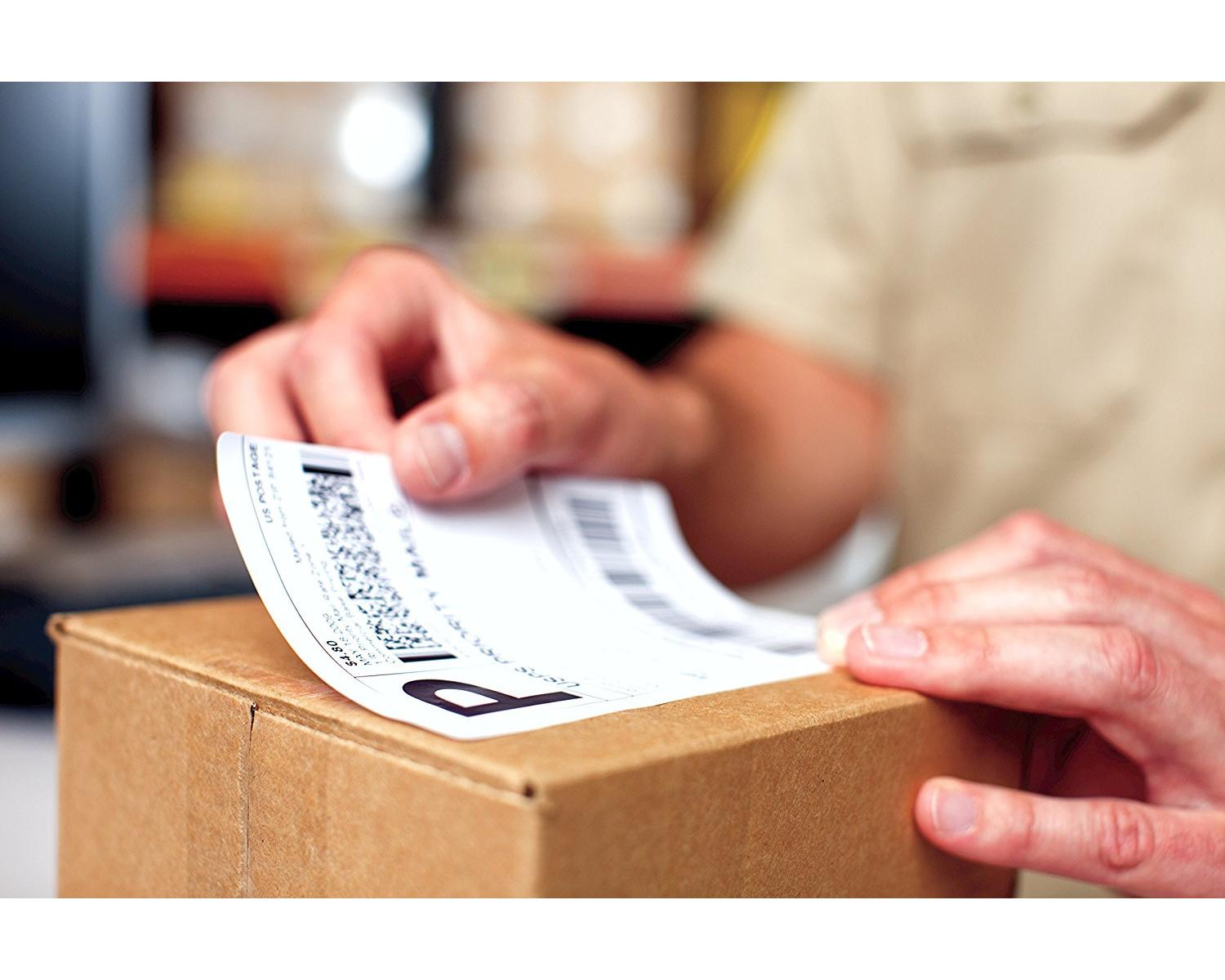 Eine Person bringt ein Priority-Mail-Etikett auf einen braunen Pappkarton in einem Raum an.