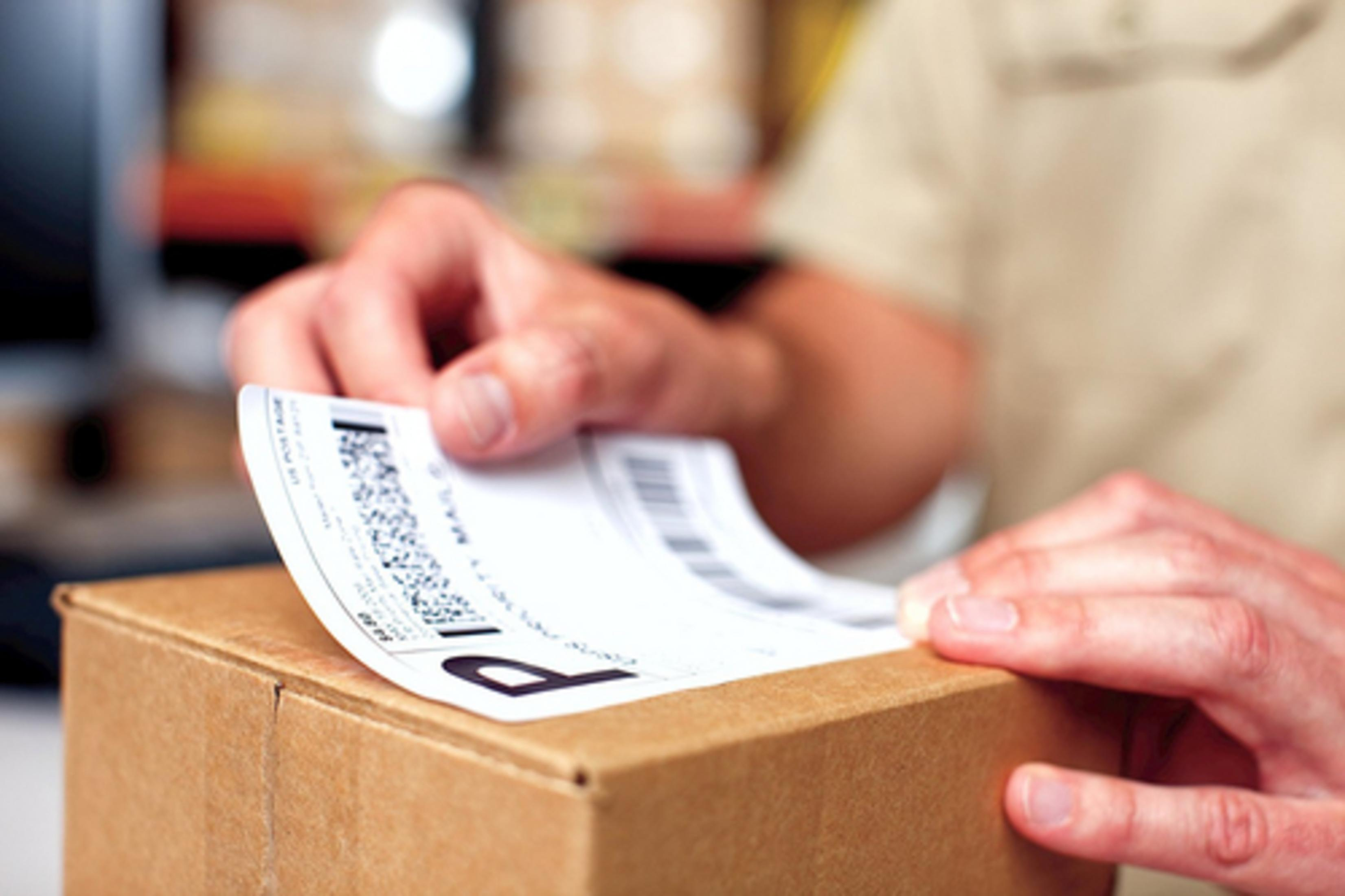 Eine Person beklebt ein Papppaket mit einem Versandetikett.