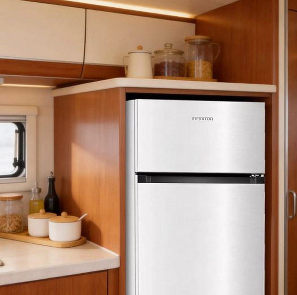Un pequeño refrigerador plateado Inﬁniton está en una cocina de autocaravana de madera con tarros encima.