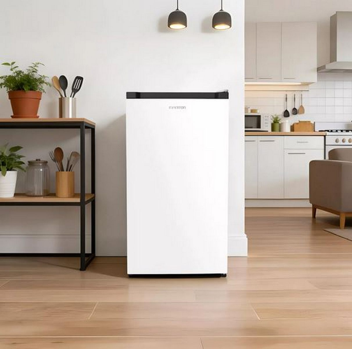 Una mini nevera blanca se encuentra en una habitación moderna con suelo de madera, junto a una estantería y cocina.